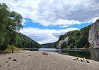 Baden an der Donau Kiesstrand an einem Fluss mit Menschen, die sich sonnen. Im Hintergrund bewaldete Hügel und Felsen.