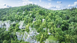 Dichte bewaldete Hügel mit zwei kleinen Gebäuden auf einem Felsvorsprung.