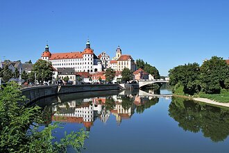 Stadtansicht mit Schloss und Brücke, Spiegelung im Fluss, blauer Himmel, Bäume am Ufer