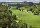 Schambachtal bei Altmannstein Tal mit grünem Gras, Bäumen, kleinem Bach und Dorf im Hintergrund unter blauem Himmel