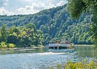 Schifffahrt durch die Weltenburger Enge Personenfähre auf Fluss vor bewaldetem Hügel bei sonnigem Himmel und Ufer mit Pflanzen im Vordergrund